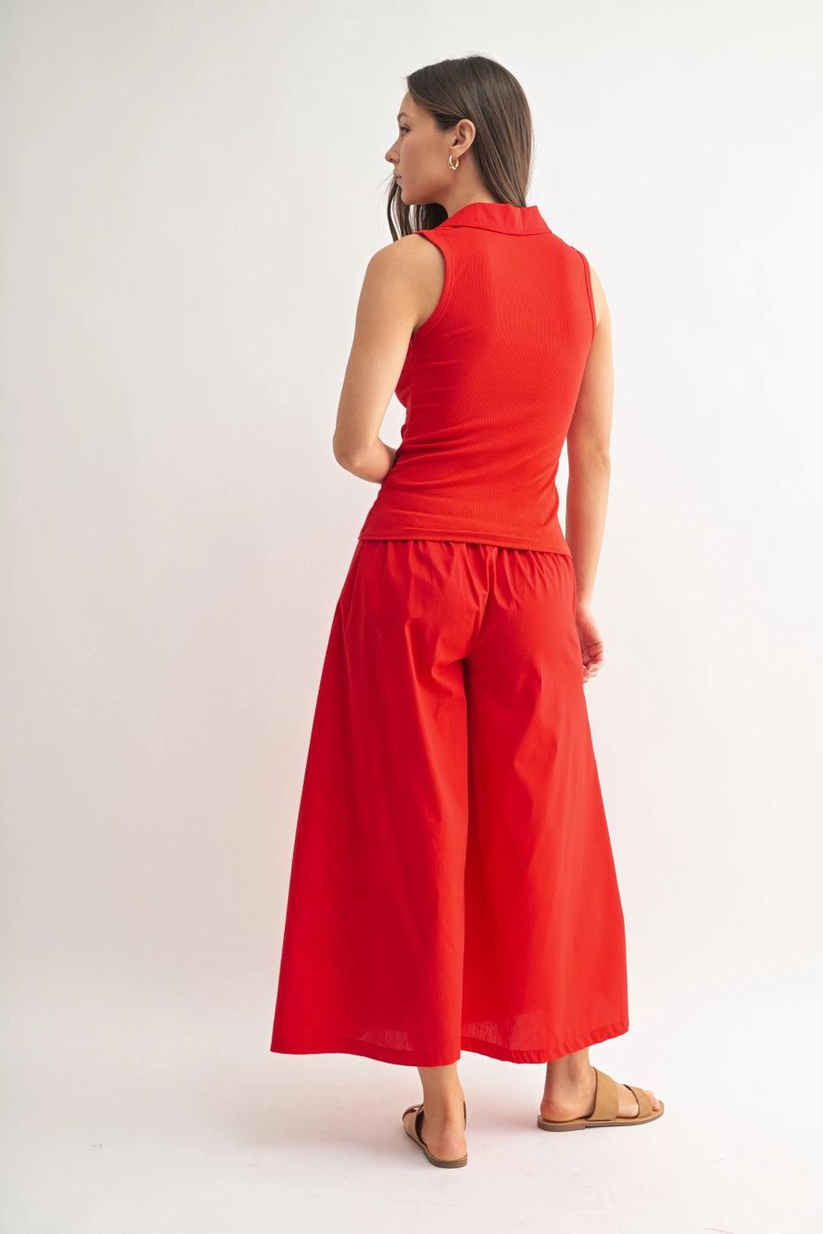 Woman wearing a red sleeveless polo top and wide-leg pants on a white background