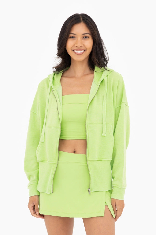Woman wearing a neon green outfit with a fleece jacket, top, and skirt on a white background
