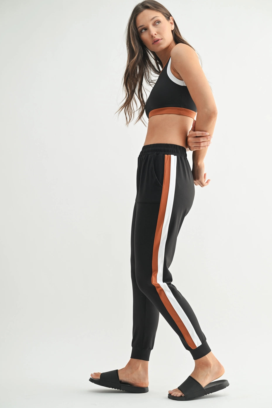 Woman wearing black athletic top and pants with white and orange stripes on a white background