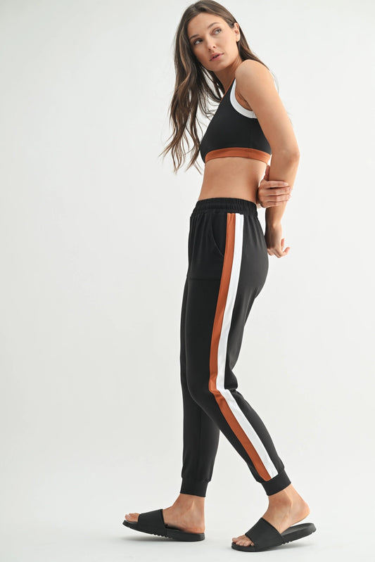 Woman wearing black athletic top and pants with white and orange stripes on a white background