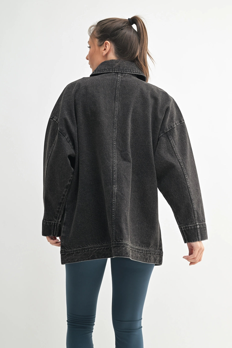 Person wearing an oversized black denim jacket on a white background