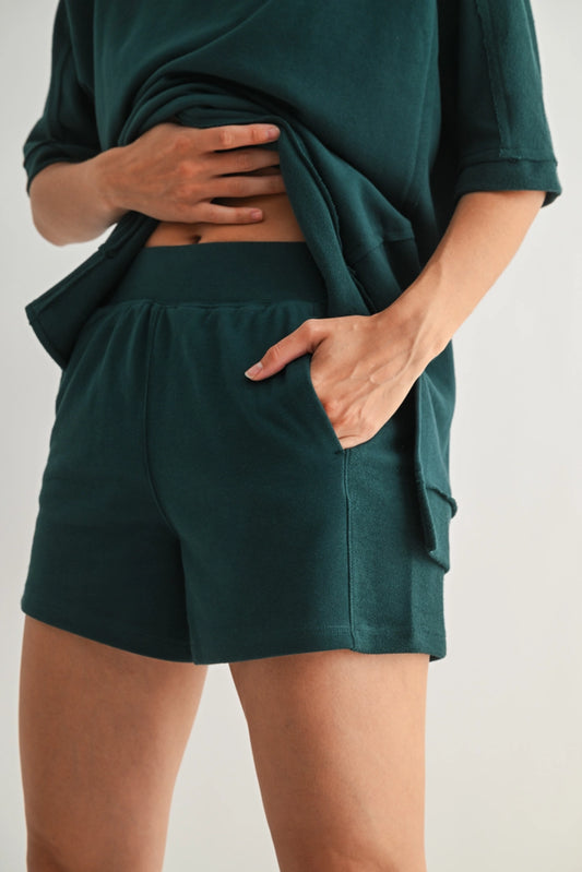 Person wearing dark green shorts and a matching top on a plain background