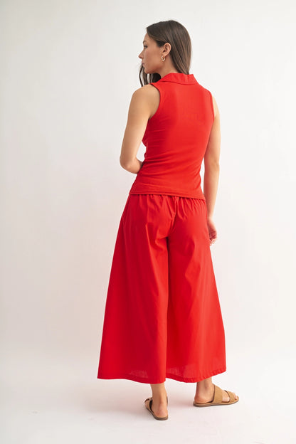 Woman wearing a red sleeveless polo top and wide-leg pants on a white background