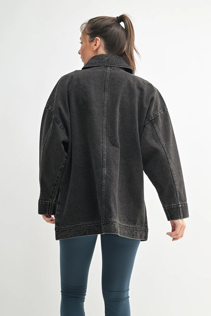 Person wearing an oversized black denim jacket on a white background